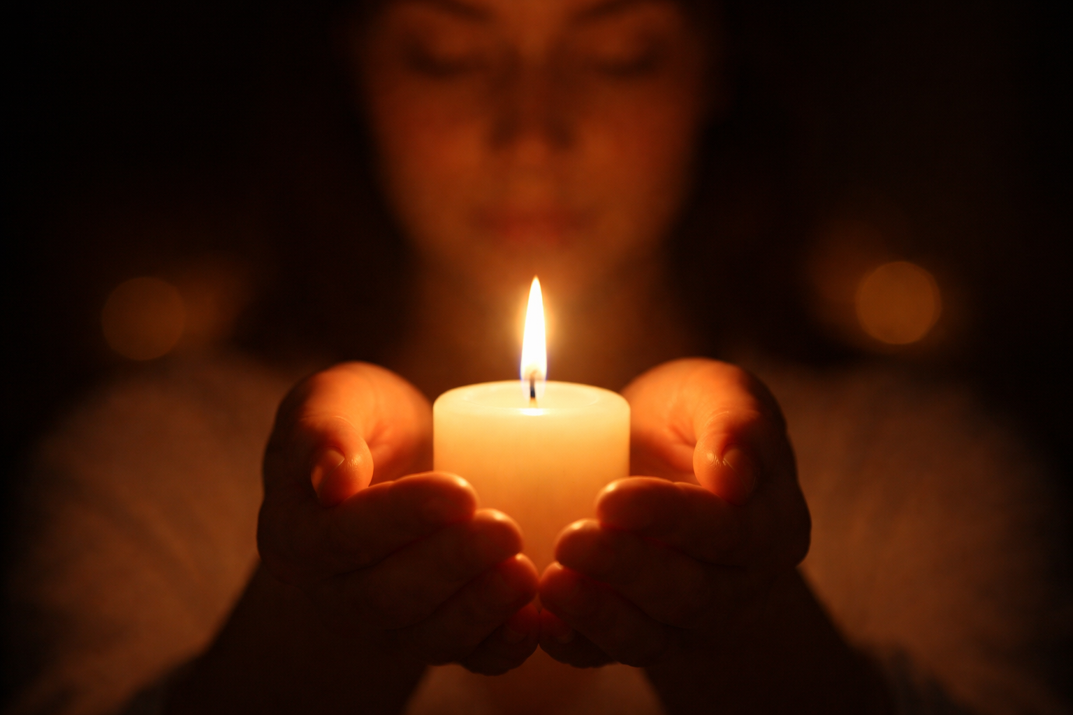 () image showing hands cupping a single white candle flame in darkness, representing the symbolic power of manifestation