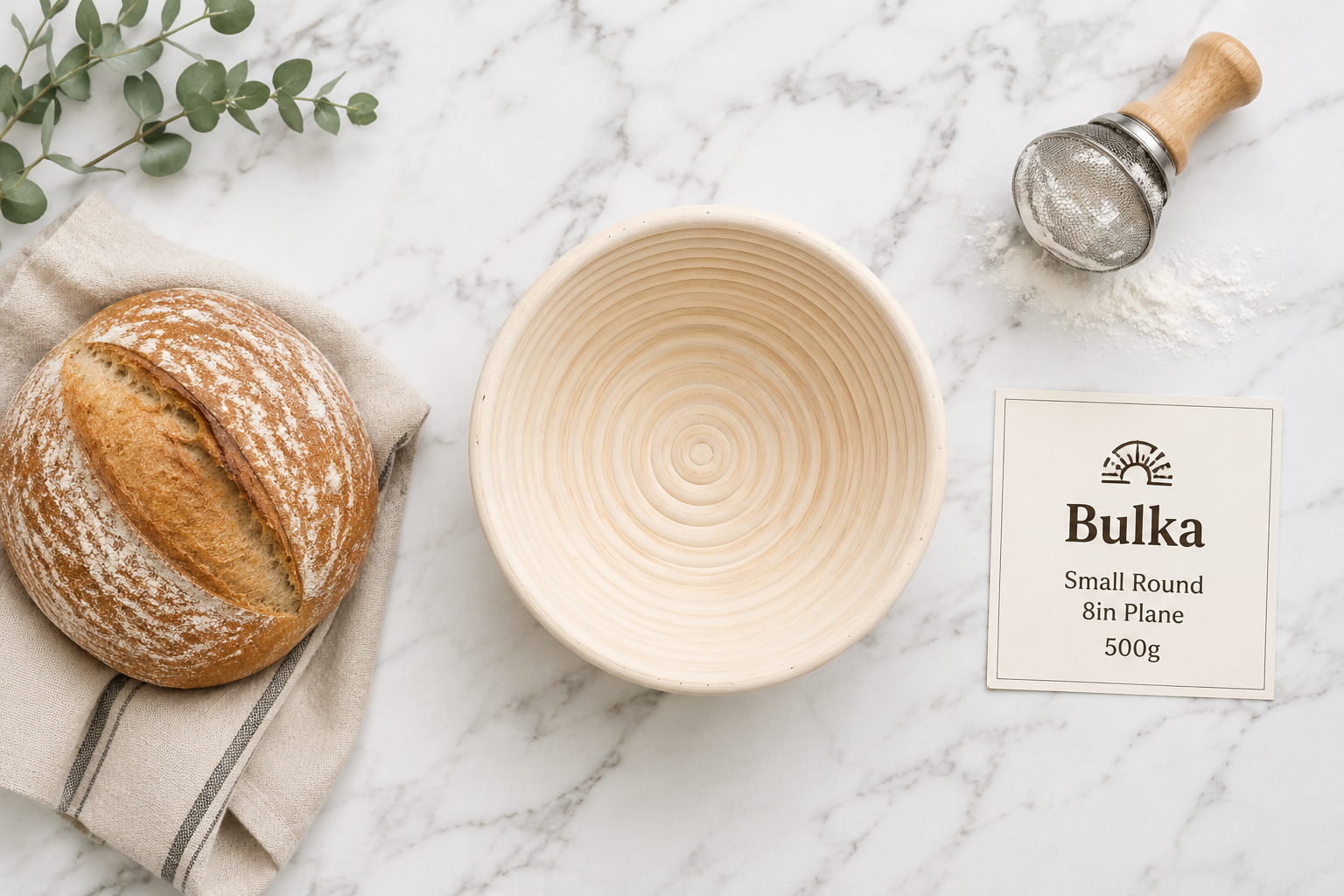 Flat-lay product image of the Bulka Wood Pulp Banneton Small Round 8 inch Plane 500g basket centered on a white marble surface, showing its smooth plain interior and compact size next to a small 500g sourdough loaf and a flour duster. Label card 'Bulka Small Round 8in Plane 500g' placed to the right. Bright, clean overhead lighting. Bulka Wood Pulp Banneton – Small Round 8" Plane 500g
