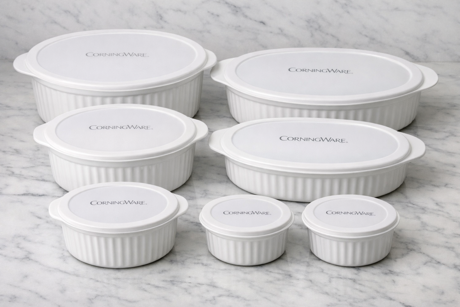 Detailed showcase of CorningWare French White 7-Pc Ceramic Bakeware Set with Lids highlighting all seven pieces arranged by size on a marble surface, showing the classic French White stoneware finish, fitted plastic lids, and CorningWare logo branding on each dish