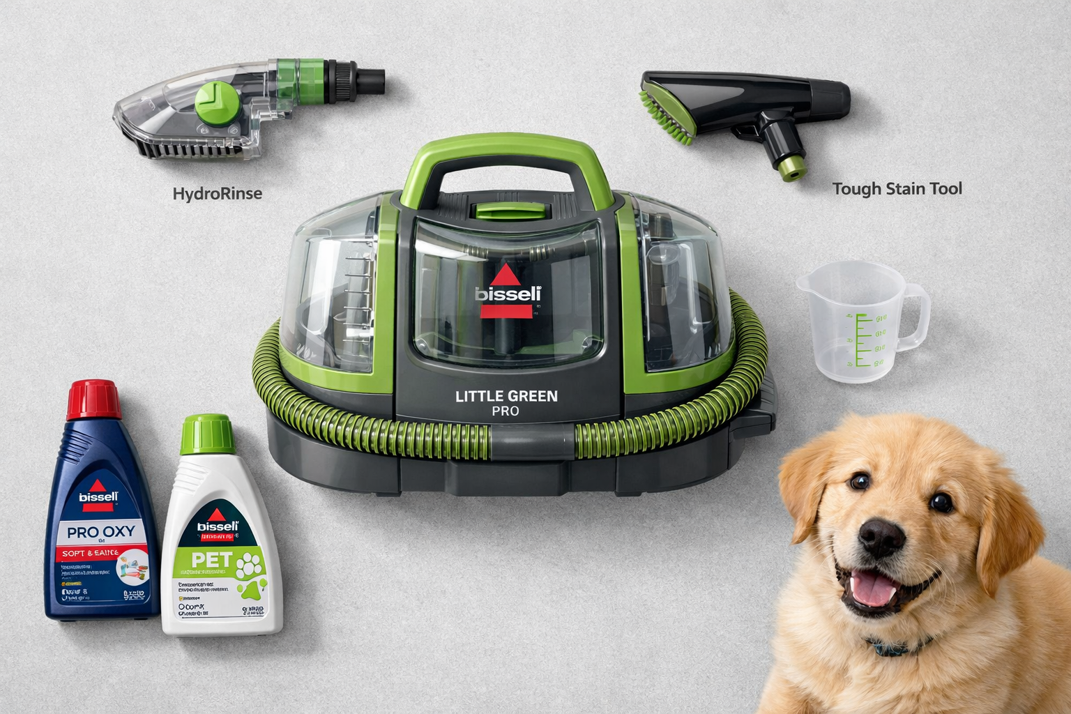 Detailed landscape format (1536x1024) editorial image showing a flat-lay overhead perspective of the Bissell Little Green Pro machine surrounded by its accessories: HydroRinse self-cleaning tool, tough stain tool, cleaning formula bottles, and a measuring cup. Items arranged neatly on a light grey surface with soft studio lighting. A small pet (golden retriever puppy) sits in the corner of the frame, referencing pet owner use case. Clean, modern product photography aesthetic with subtle green color accents throughout the composition. 