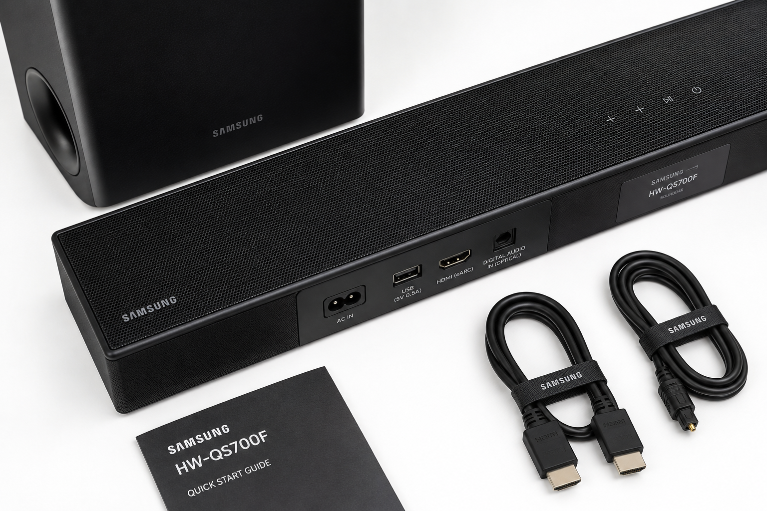 Detailed landscape format (1536x1024) showing a close-up overhead flat-lay of the Samsung HW-QS700F soundbar and wireless subwoofer on a clean white surface, with connectivity ports visible, HDMI and optical cables neatly arranged beside the unit, Samsung branding visible, soft studio lighting from above, product photography style, sharp detail on speaker grille texture, deep black and white color palette
